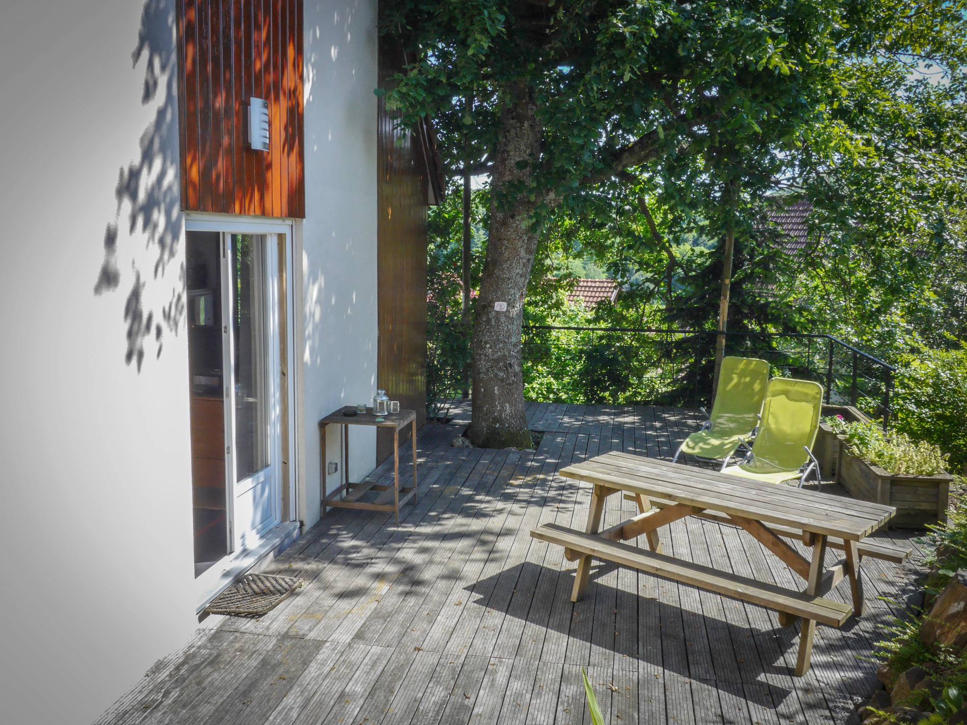 Terrasse privée en bois des Terrasses du Zimmerberg, avec table, transats à l’ombre d’un chêne